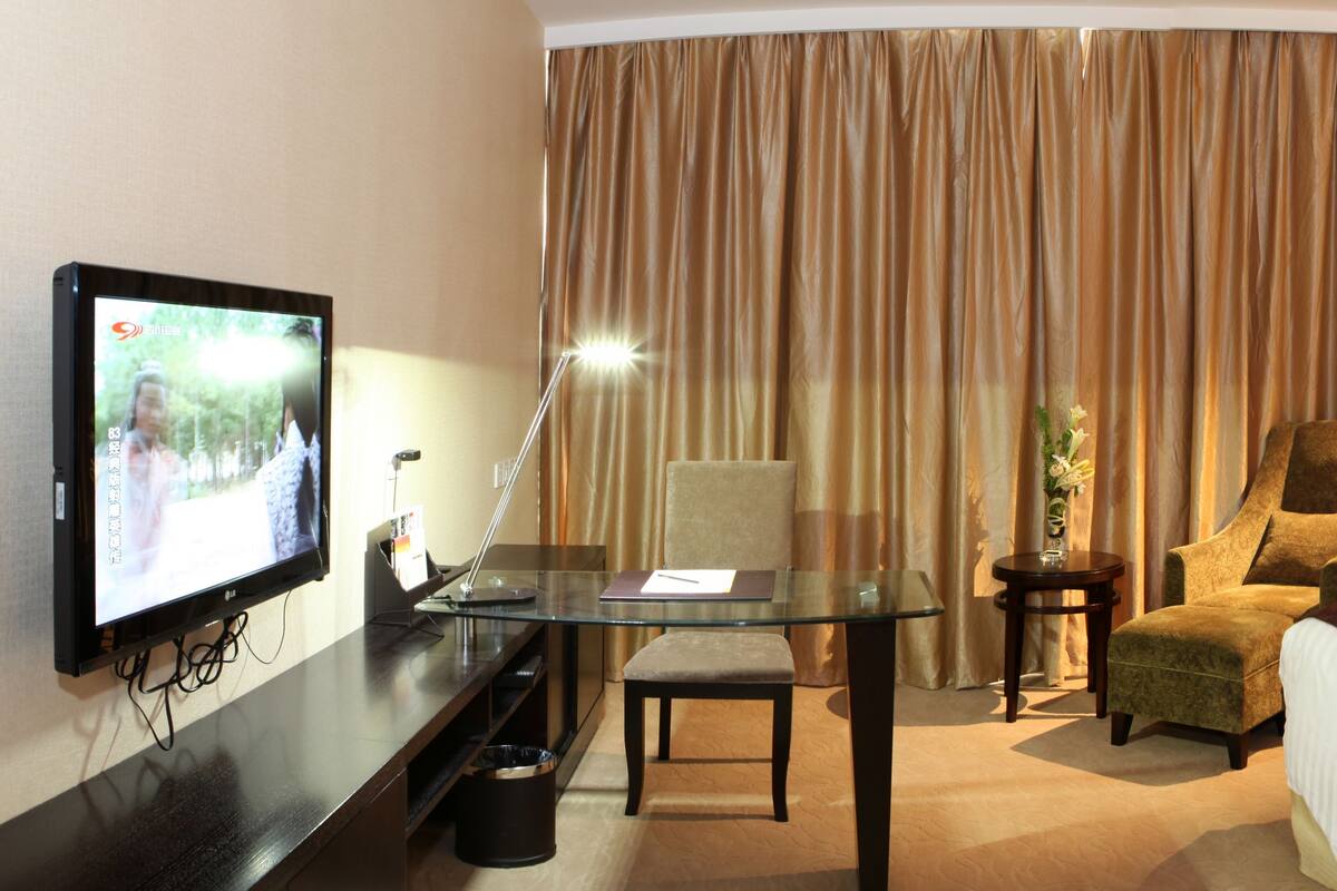 Una habitación de hotel con cama, escritorio, computadora, silla, televisor y cortinas.