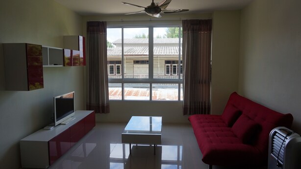A living room with a TV on a white cabinet, a red sofa, a glass coffee table, and a ceiling fan. - GIB Apartment (Surin)
