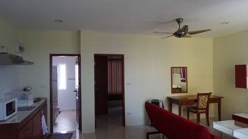 A room with a kitchenette, a dining area with a chair and table, a ceiling fan, and a door leading to another room.