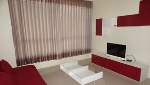 A modern living room with a red sofa, a glass coffee table, a flat-screen TV, and a red and white cabinet. - GIB Apartment (Surin)