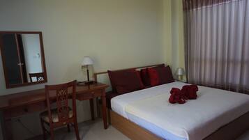 Une chambre d’hôtel avec un lit, un bureau, une chaise, une lampe et une fenêtre avec des rideaux.