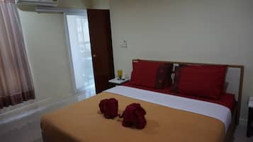 A hotel room with a bed, two red towels, a nightstand, a lamp, and an air conditioning unit.
