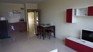 A modern kitchen with a microwave, refrigerator, and cabinets. There is a dining area with a table and chairs, and a TV on a stand. - GIB Apartment (Surin)