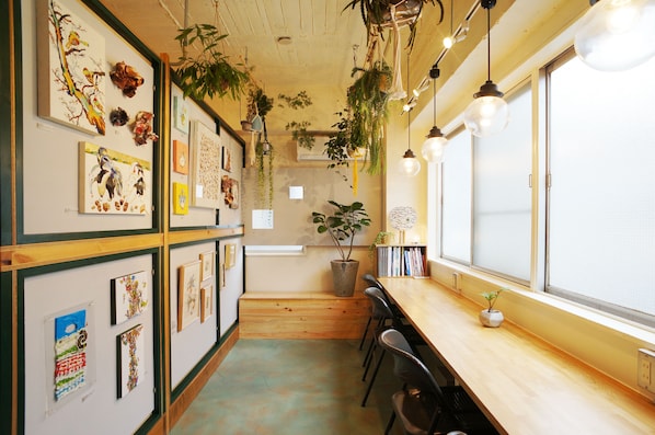 A room with a wooden bench, a long table, and multiple framed artworks on the walls. - Guest House Denchi - Hostel (Tokyo)