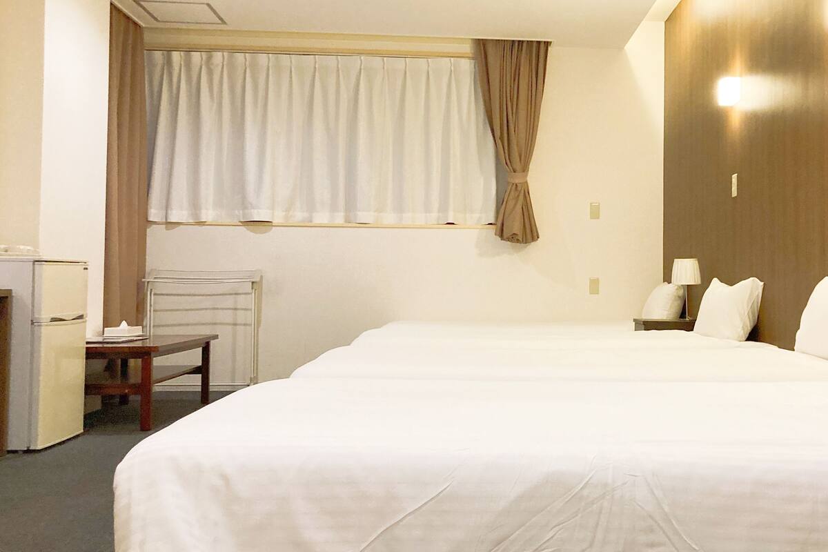 Une chambre d’hôtel avec un grand lit, un bureau, une chaise, une fenêtre avec des rideaux et une lampe fixée au mur.