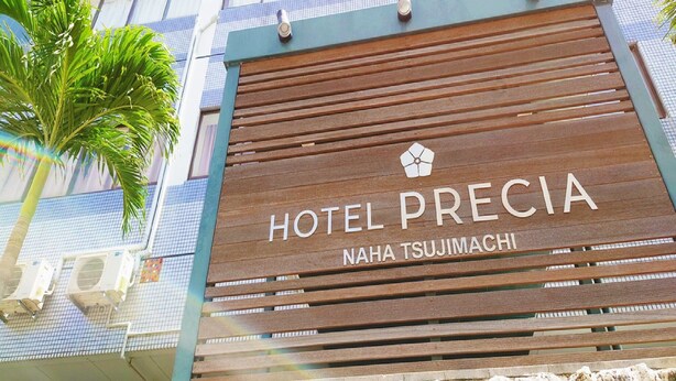 Une enseigne d’hôtel portant les noms « HOTEL PRECIA » et « NAHA TSUJIMACHI ».