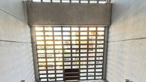 Une pièce avec un plancher en bois, un mur en béton et une fenêtre ornée d’une grille métallique.