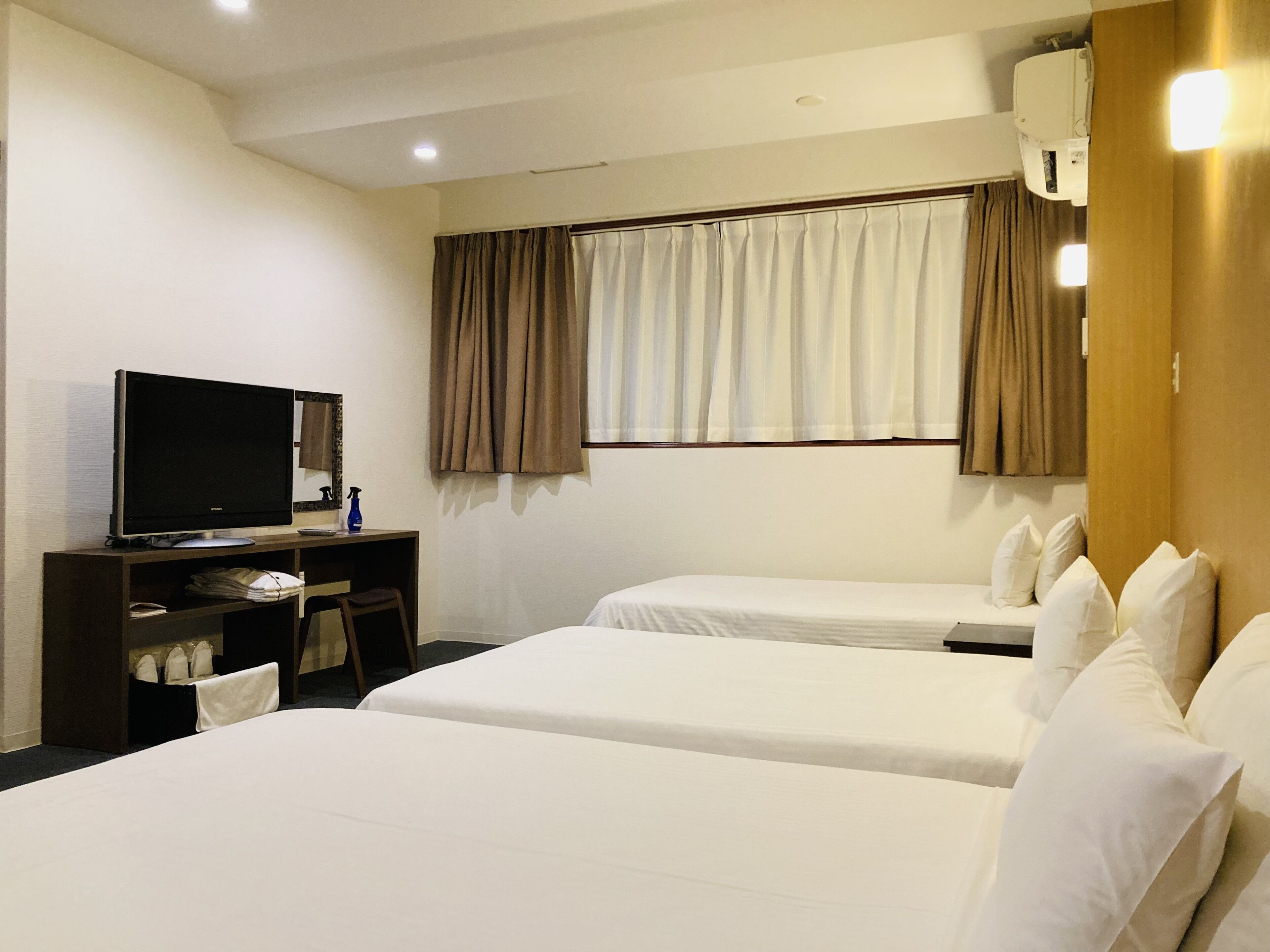 A hotel room with two beds, a desk with a television, and a window with curtains.