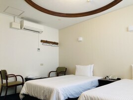 Quarto de hotel com duas camas, uma escrivaninha, uma cadeira, ar condicionado, um cabideiro e um telefone.