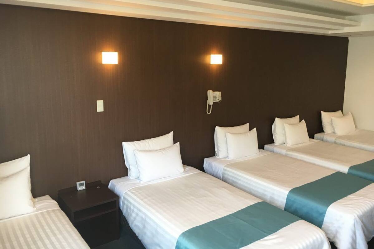 Une chambre d’hôtel avec quatre lits, un téléphone fixé au mur et une table de chevet avec une horloge.
