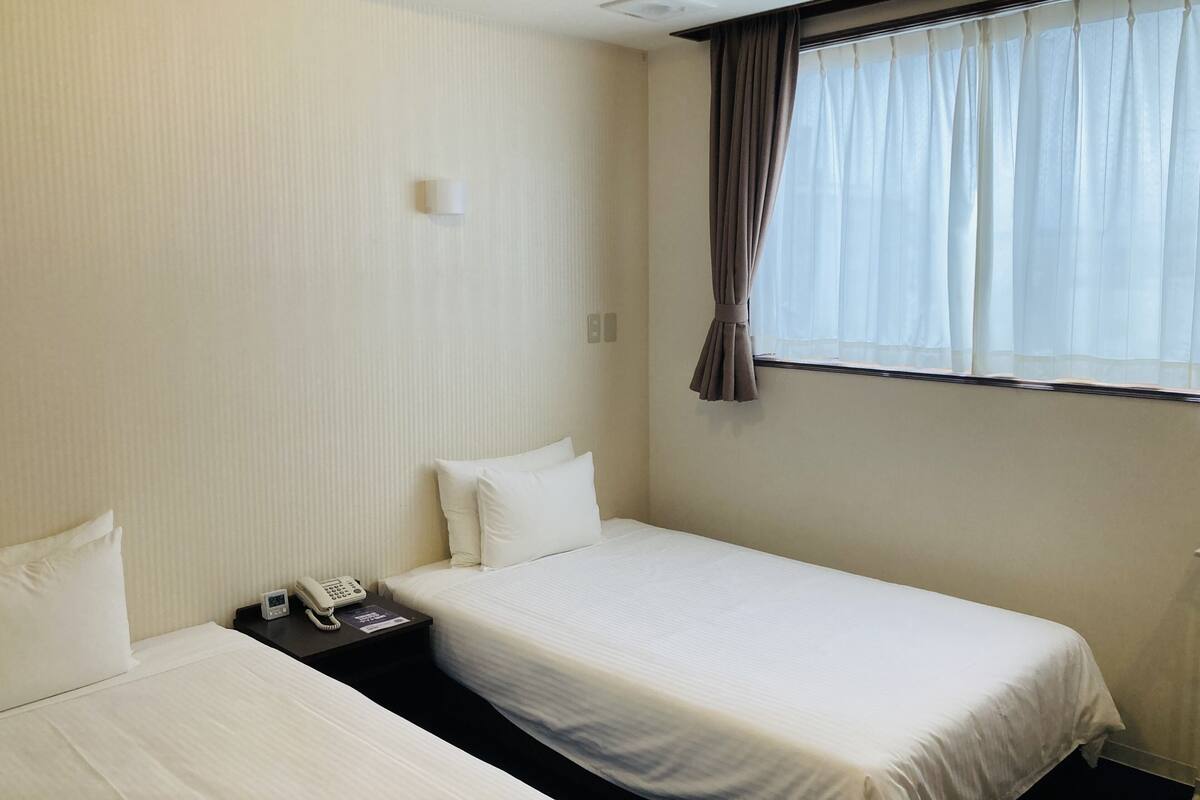 Une chambre d’hôtel avec deux lits simples, une table de chevet avec un téléphone et une fenêtre avec des rideaux.