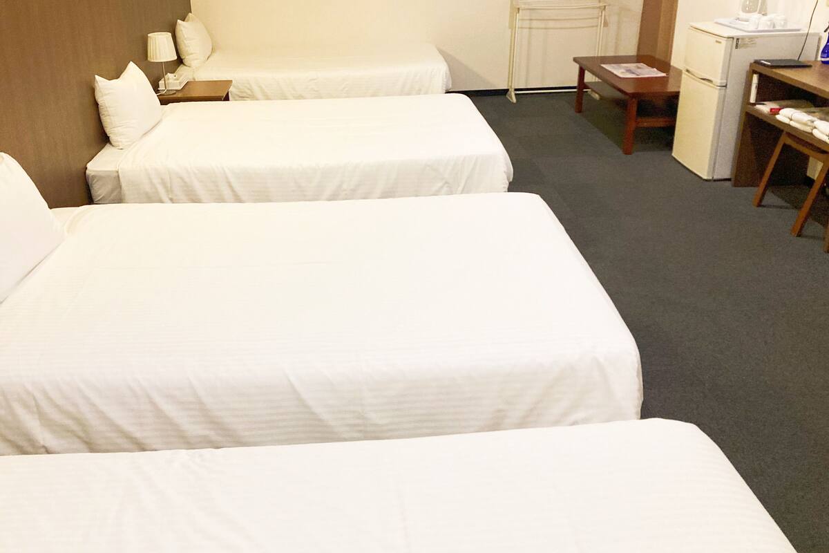 Une chambre d’hôtel avec deux lits simples, une petite table, une chaise, un bureau et un réfrigérateur.