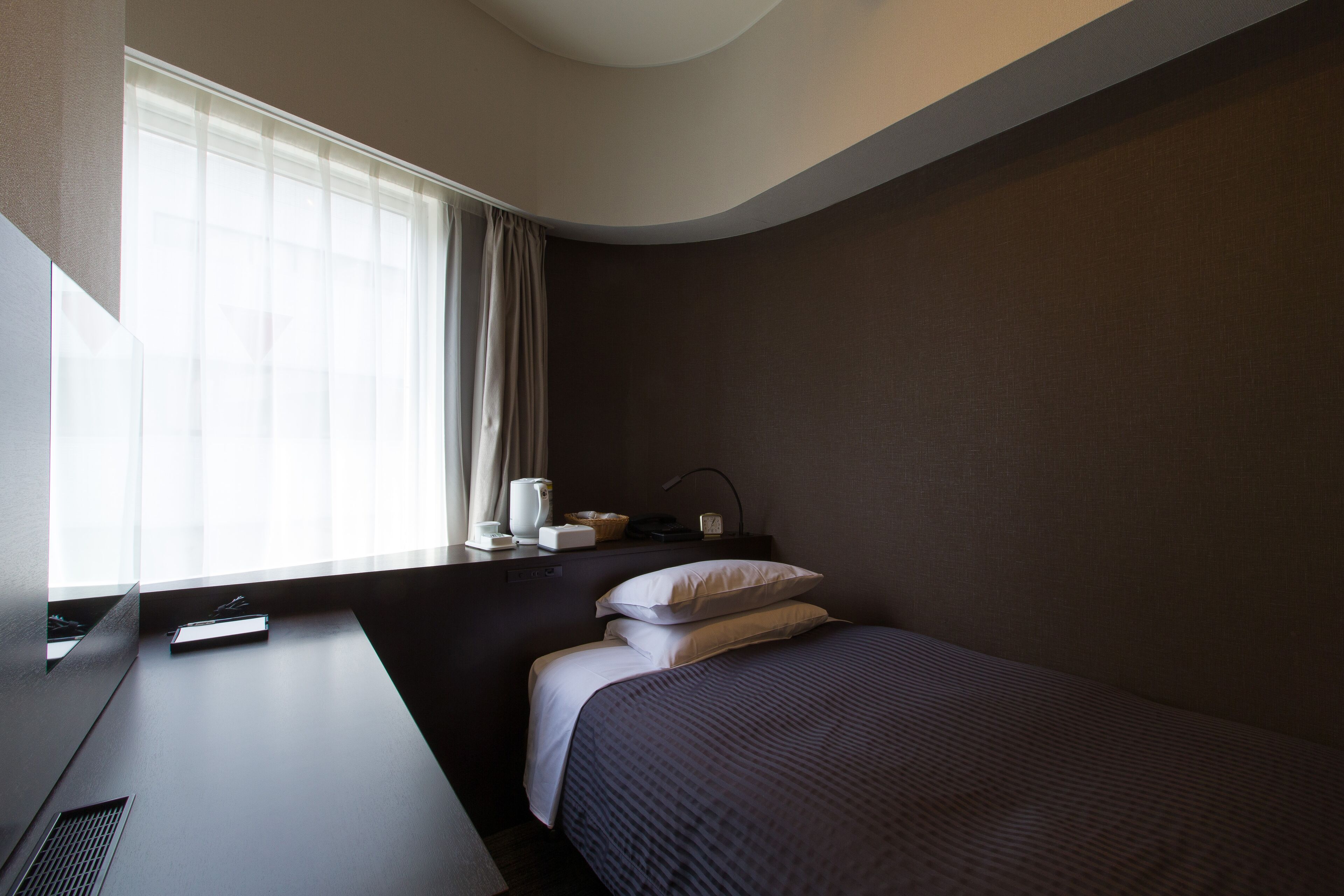 Een moderne hotelkamer met een bed, een bureau en een raam met gordijnen.