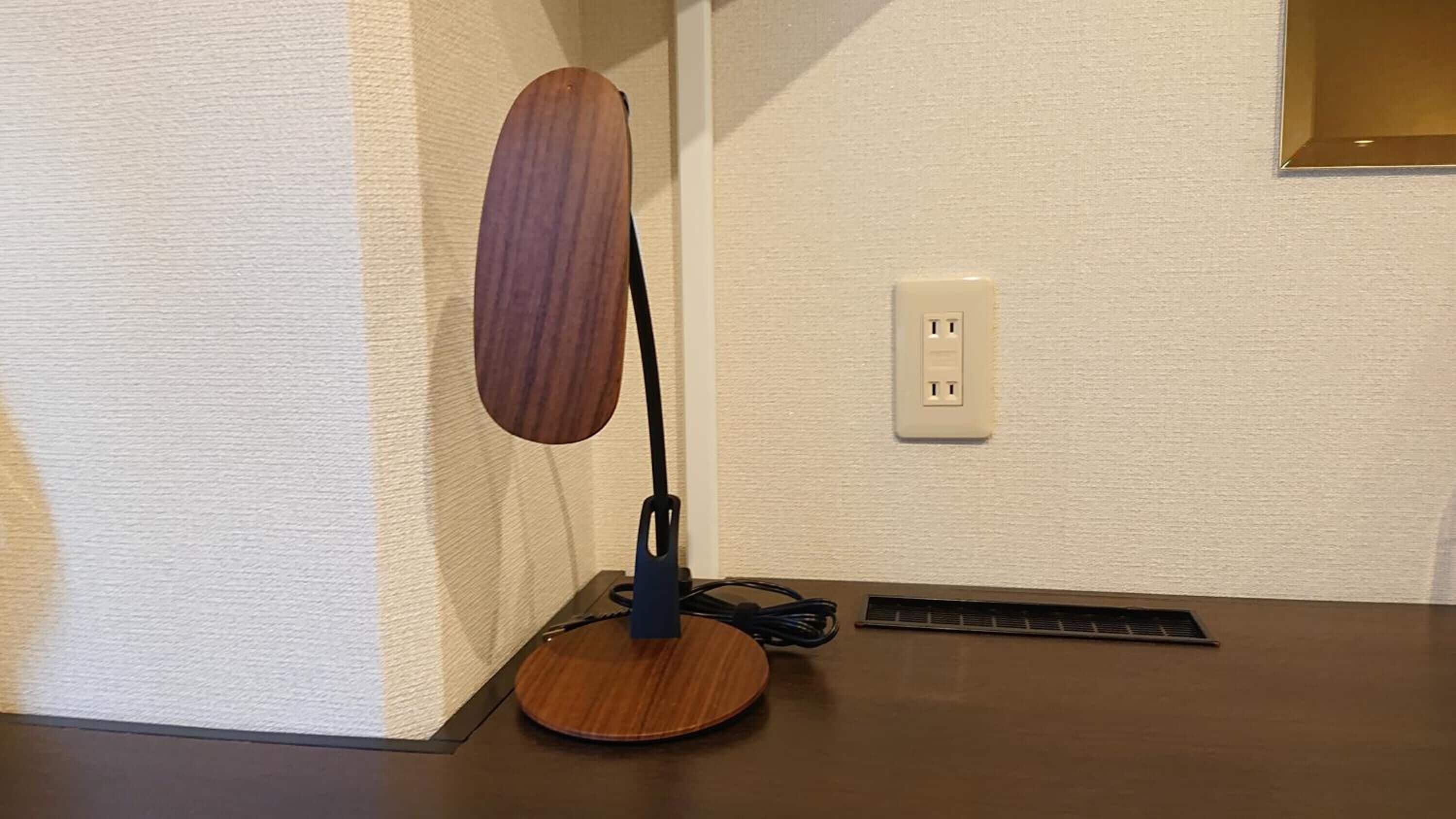 A wooden desk lamp with a cord plugged into a wall socket.