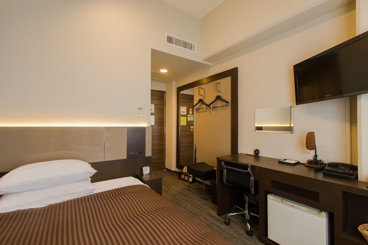 A hotel room with a bed, desk, chair, and a television.