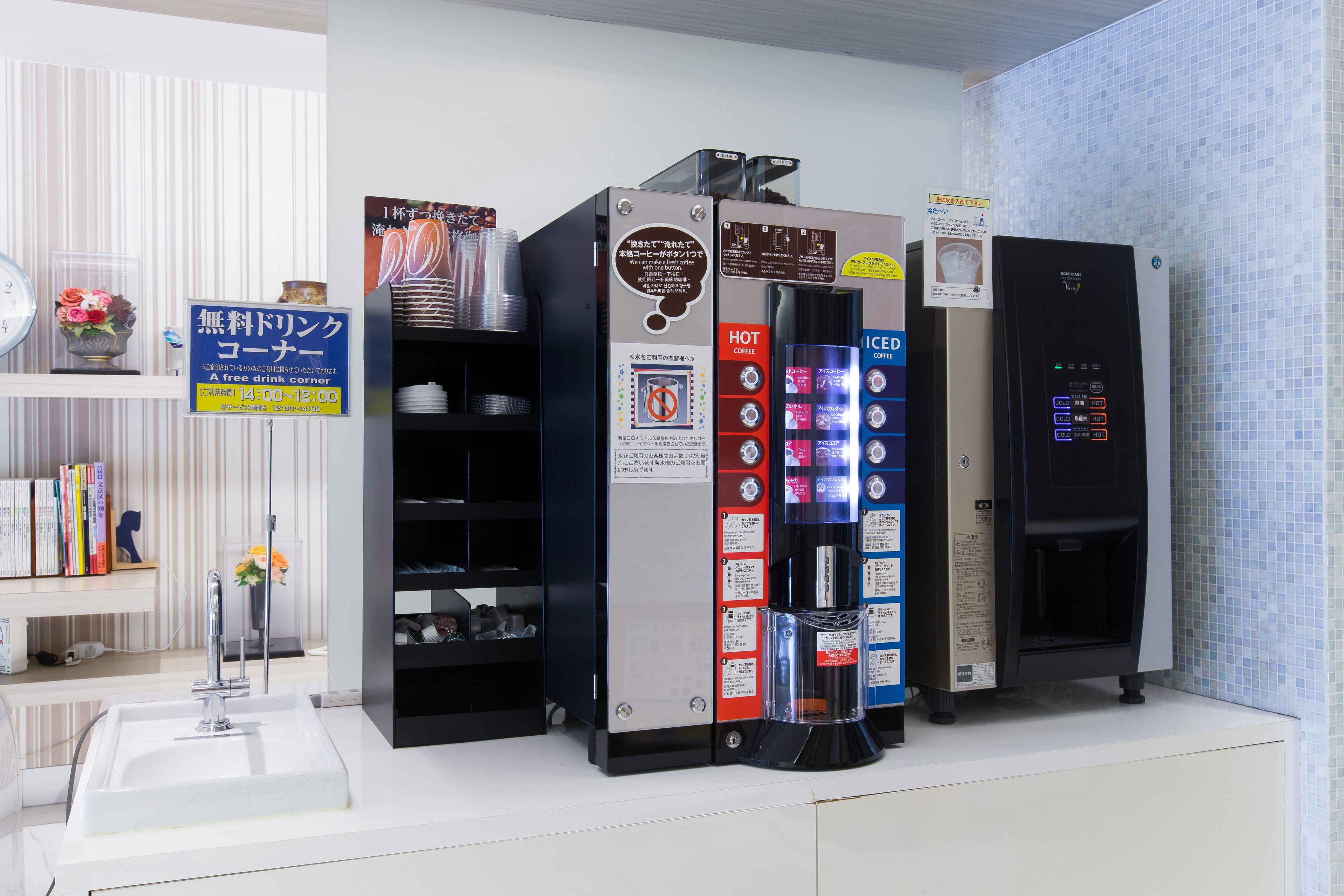A coffee machine with a digital interface, a free drink corner sign, and a shelf with books and flowers.