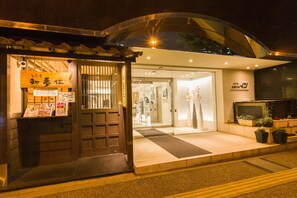 A hotel entrance with a traditional wooden door, a reception area, and potted plants on the sidewalk. - Ochanomizu Inn (Tokyo)