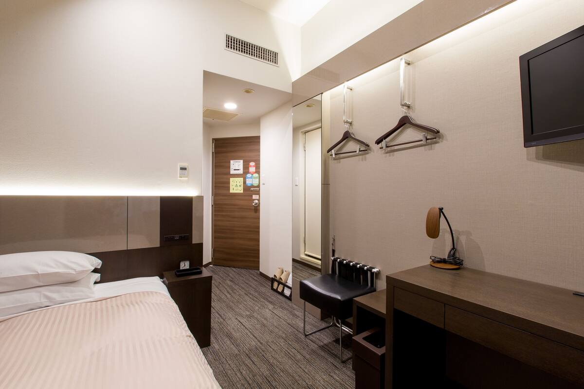 A hotel room with a bed, a desk, a chair, a mirror, and a TV.
