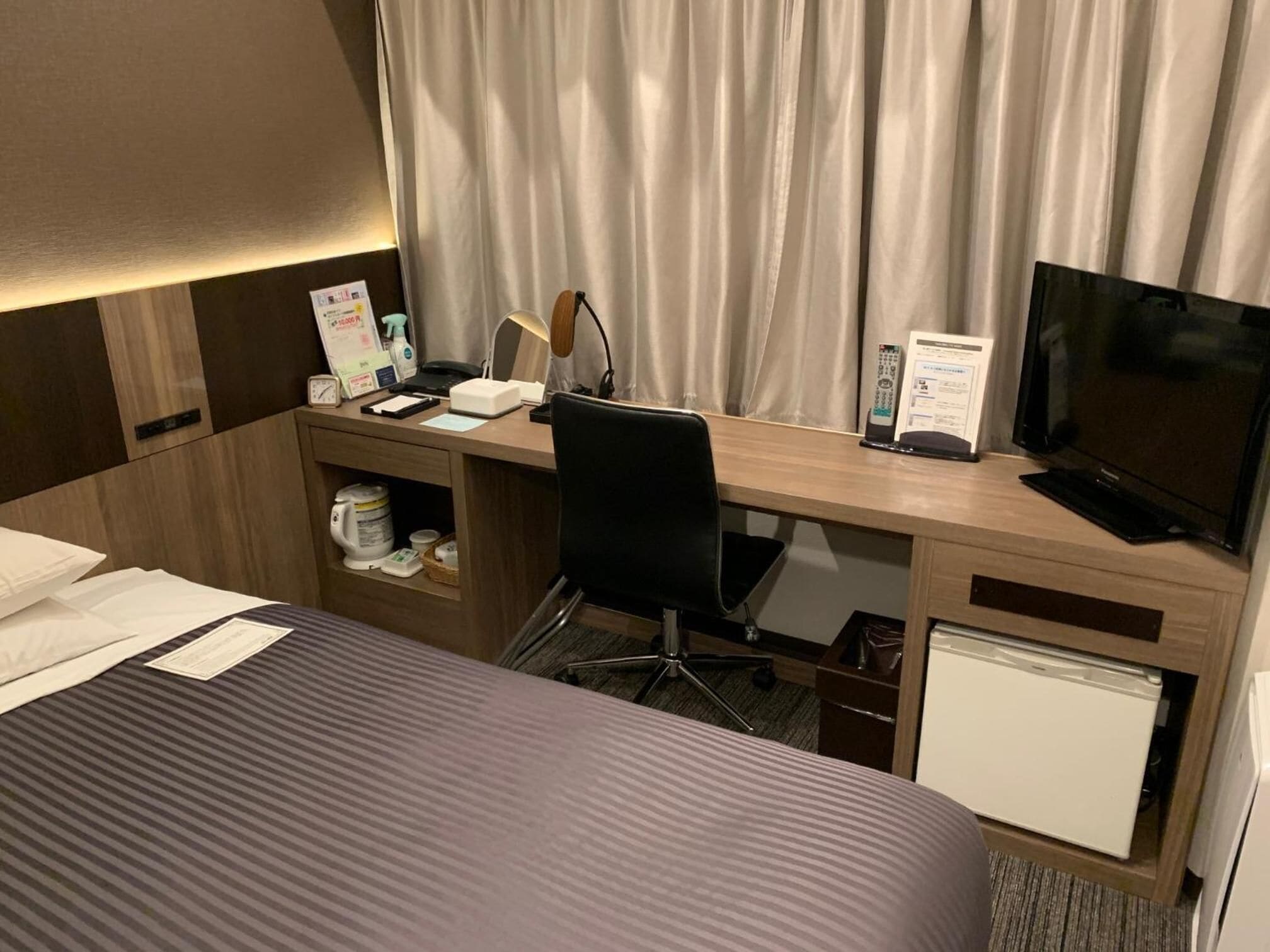 Een hotelkamer met een bed, een bureau met een computer, een televisie en een minibar.