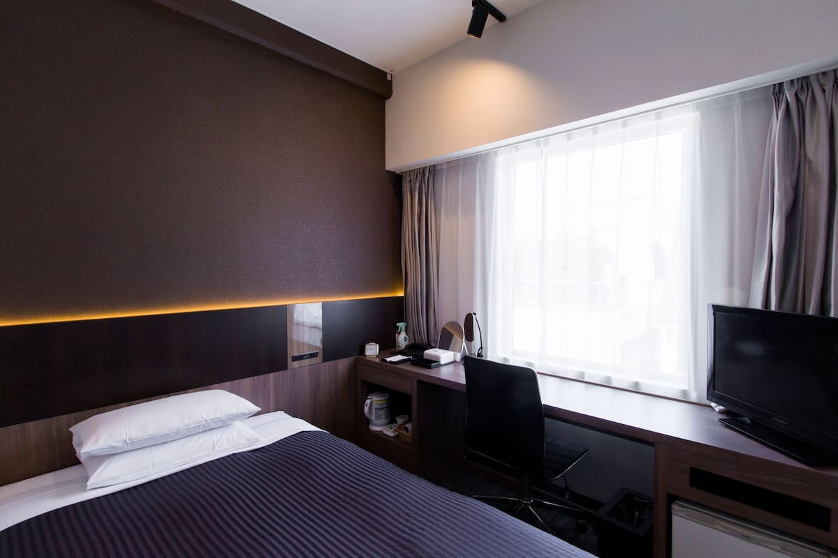 A hotel room with a bed, a desk with a computer, a TV, and a window with curtains.