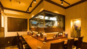 A restaurant with a long wooden counter, multiple chairs, and a large window overlooking the kitchen. - Ochanomizu Inn (Tokyo)