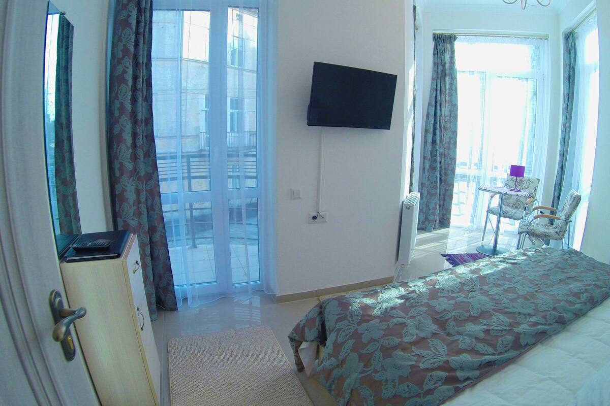Une chambre d’hôtel avec un lit, un téléviseur fixé au mur, un bureau avec une chaise et une vue sur l’extérieur par la fenêtre.
