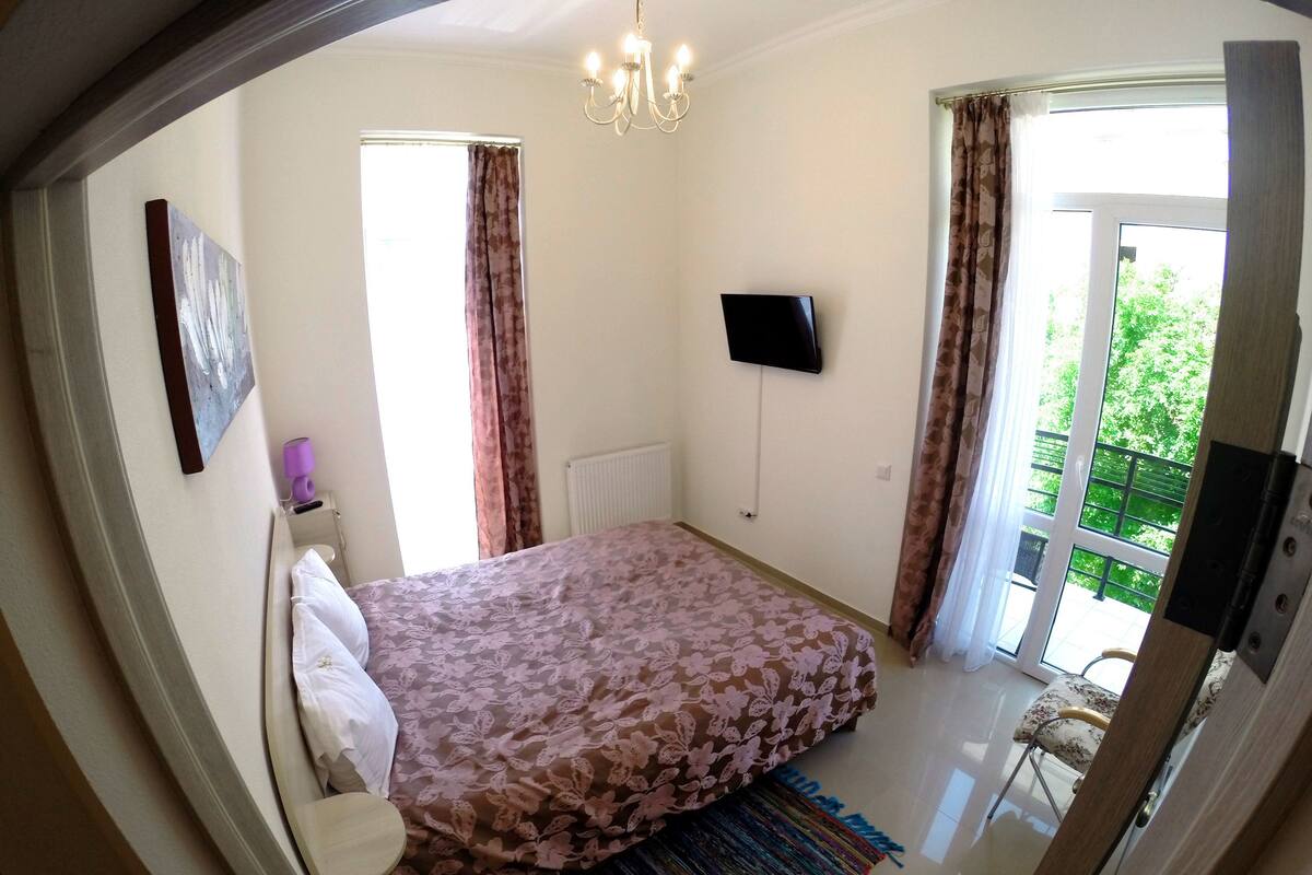 Une chambre à coucher avec un lit, une télévision, une fenêtre et une porte donnant sur un balcon.
