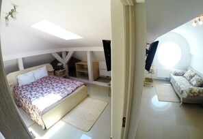 A bedroom with a bed, a desk, a chair, a TV, and a window.