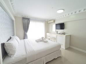 Een hotelkamer met een opgemaakt bed, een bureau met een flatscreen televisie, en een raam met gordijnen.