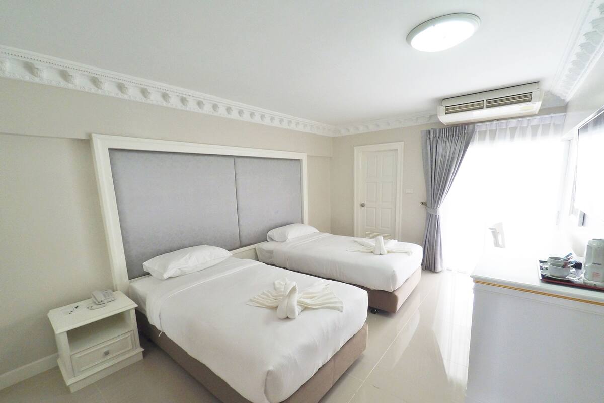 Une chambre d’hôtel avec deux lits, une table de chevet, un appareil de climatisation et une fenêtre avec des rideaux.