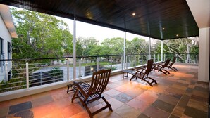 Un espace extérieur aménagé, abrité et doté de chaises et d’une table, de grandes fenêtres et d’une vue sur les arbres.