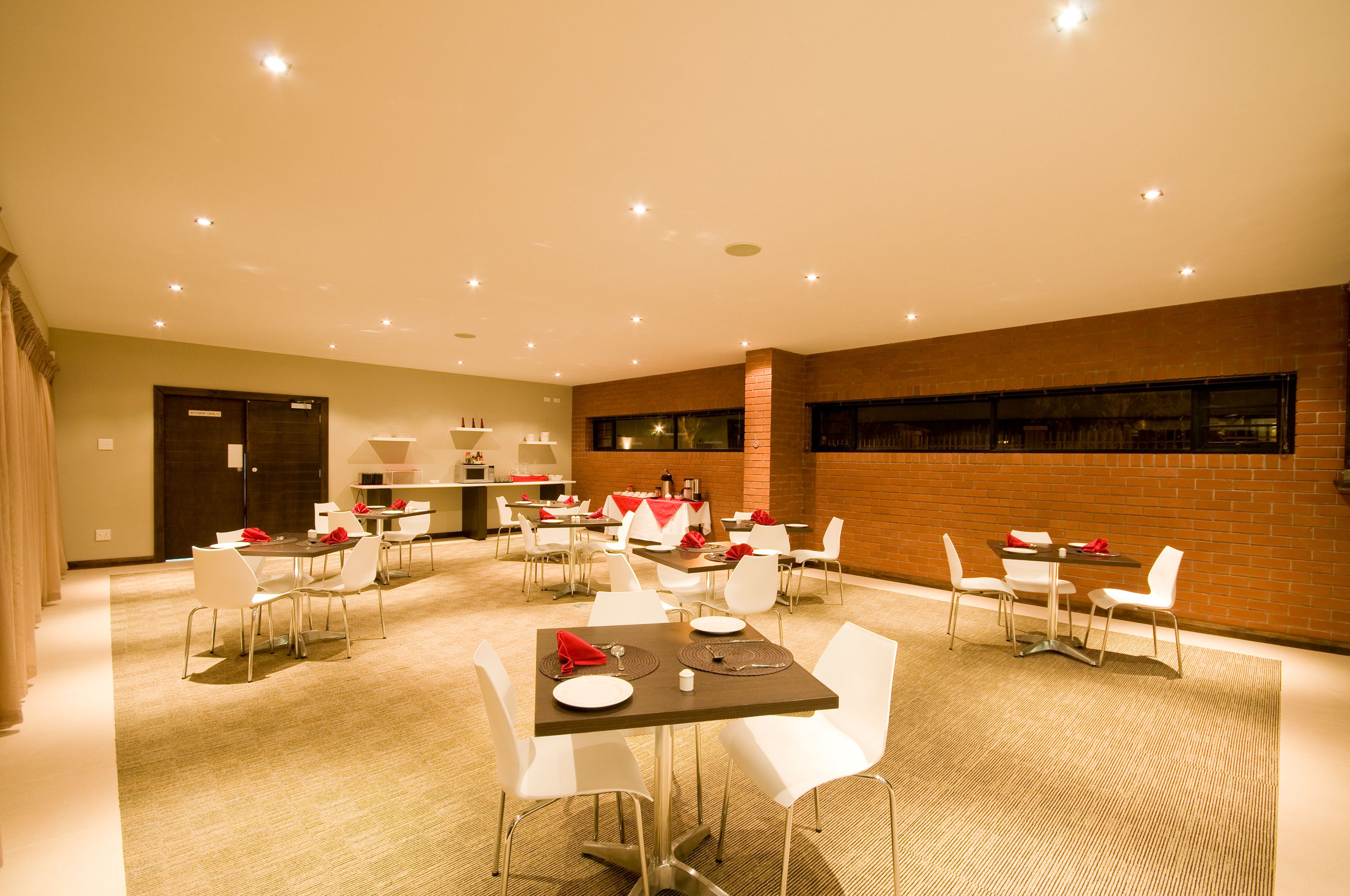 Een restaurantgedeelte in een hotel, met meerdere tafels en stoelen, een bakstenen muur en een vloerkleed.