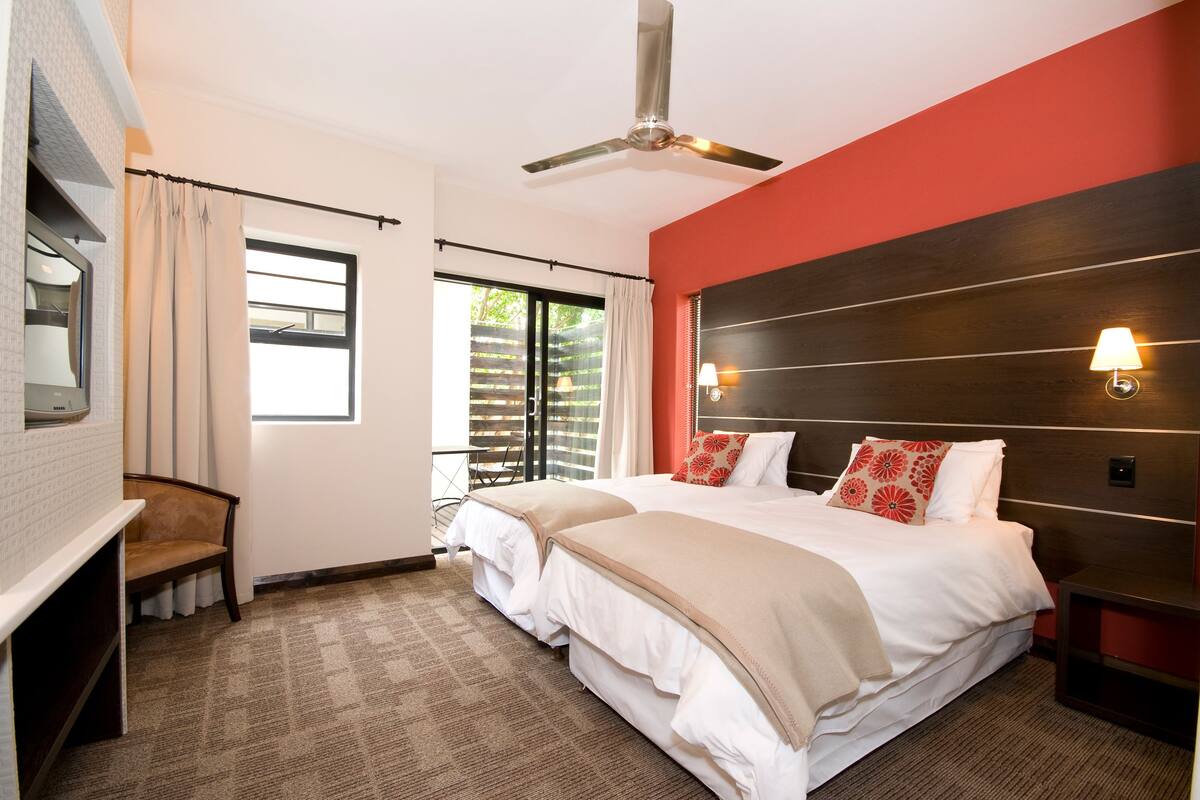 A hotel room with a large bed, two bedside tables, a ceiling fan, a TV, and a window with curtains.