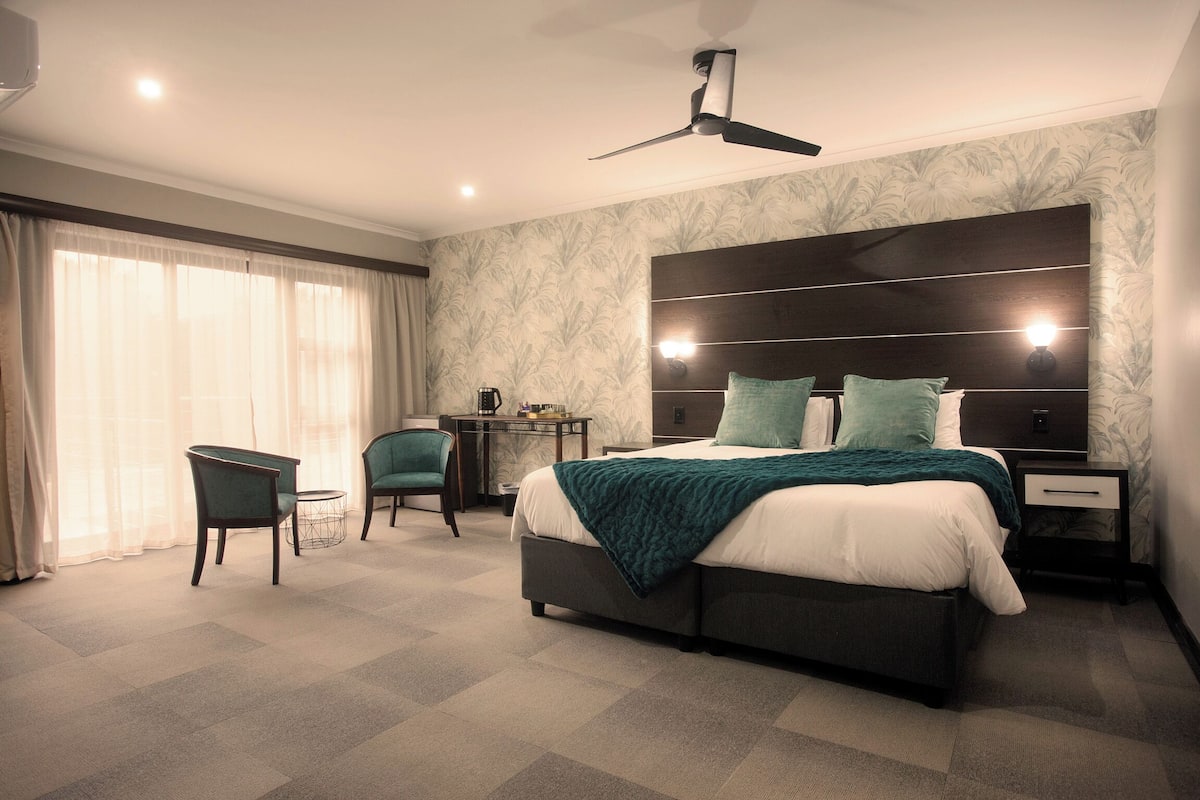A modern hotel room with a large bed, a desk, a chair, and a ceiling fan.