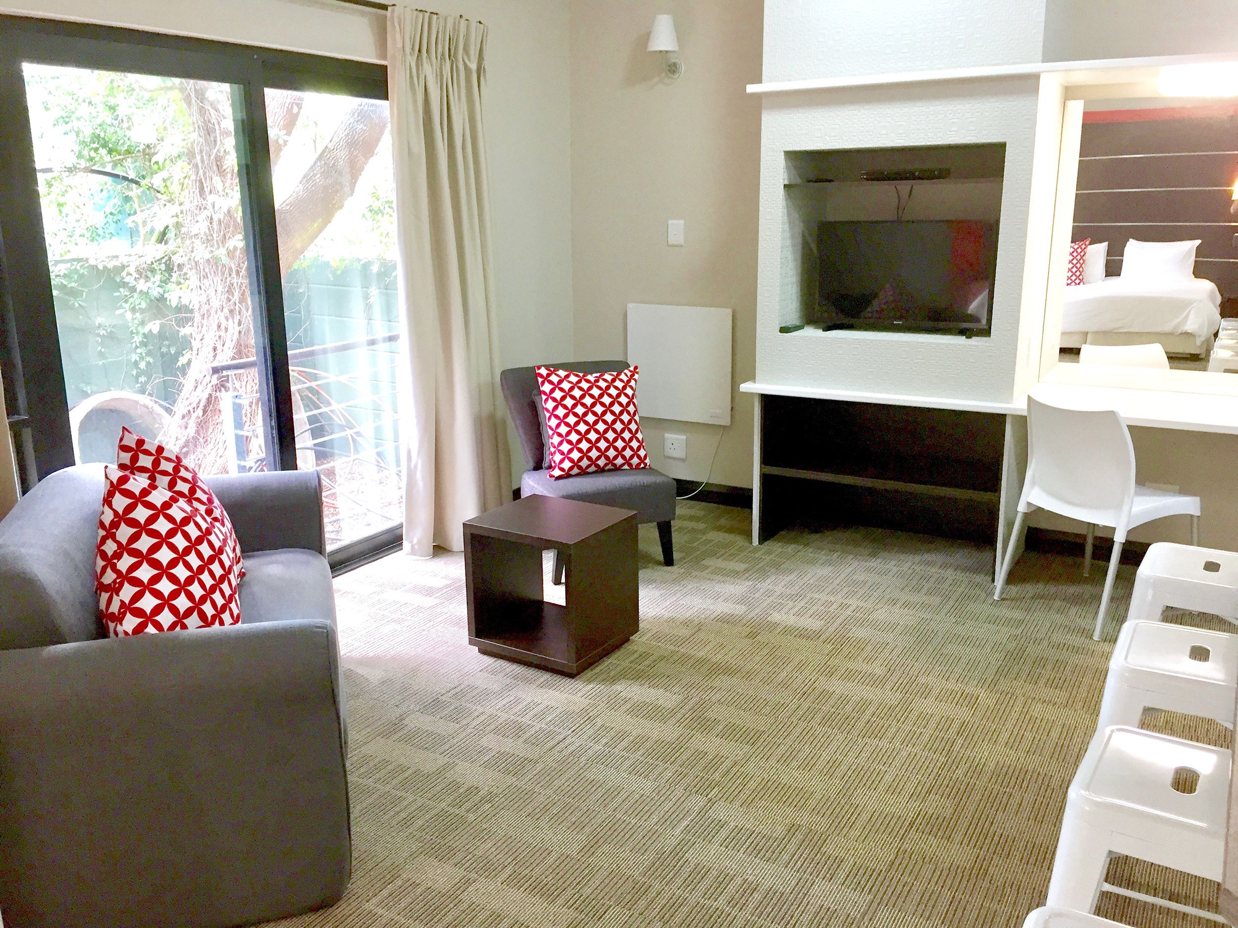 Habitación de hotel con un sofá gris, una mesita de café oscura y un escritorio blanco, además de un televisor.