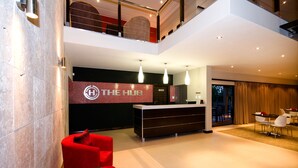 Un hall d’hôtel moderne avec un comptoir d’accueil, des chaises rouges, un escalier et une vue sur l’extérieur.