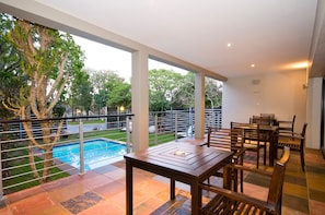 Un balcón amplio con piscina, muebles de madera y vistas al entorno verde.