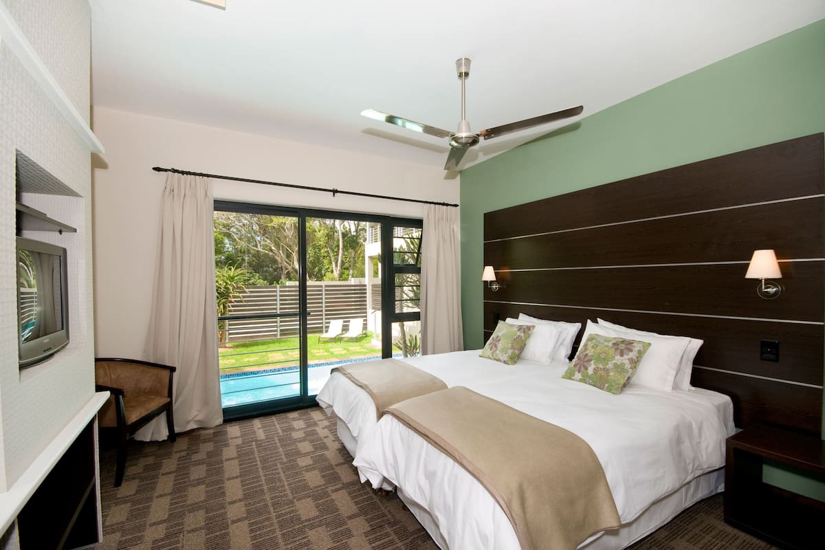 A hotel room with a large bed, a ceiling fan, a TV, and a view of the outdoors.