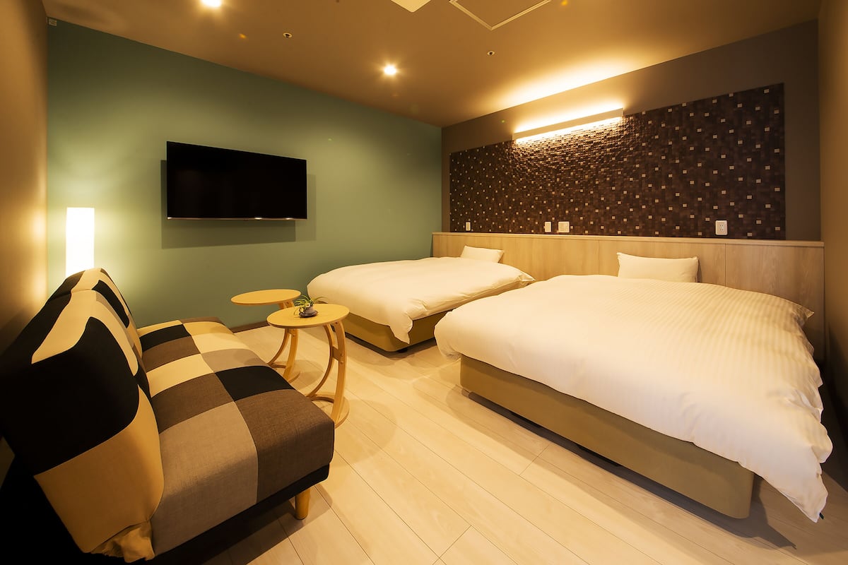 Ein Hotelzimmer mit zwei Betten, einem Sofa, einem Fernseher und einer Wandleuchte.