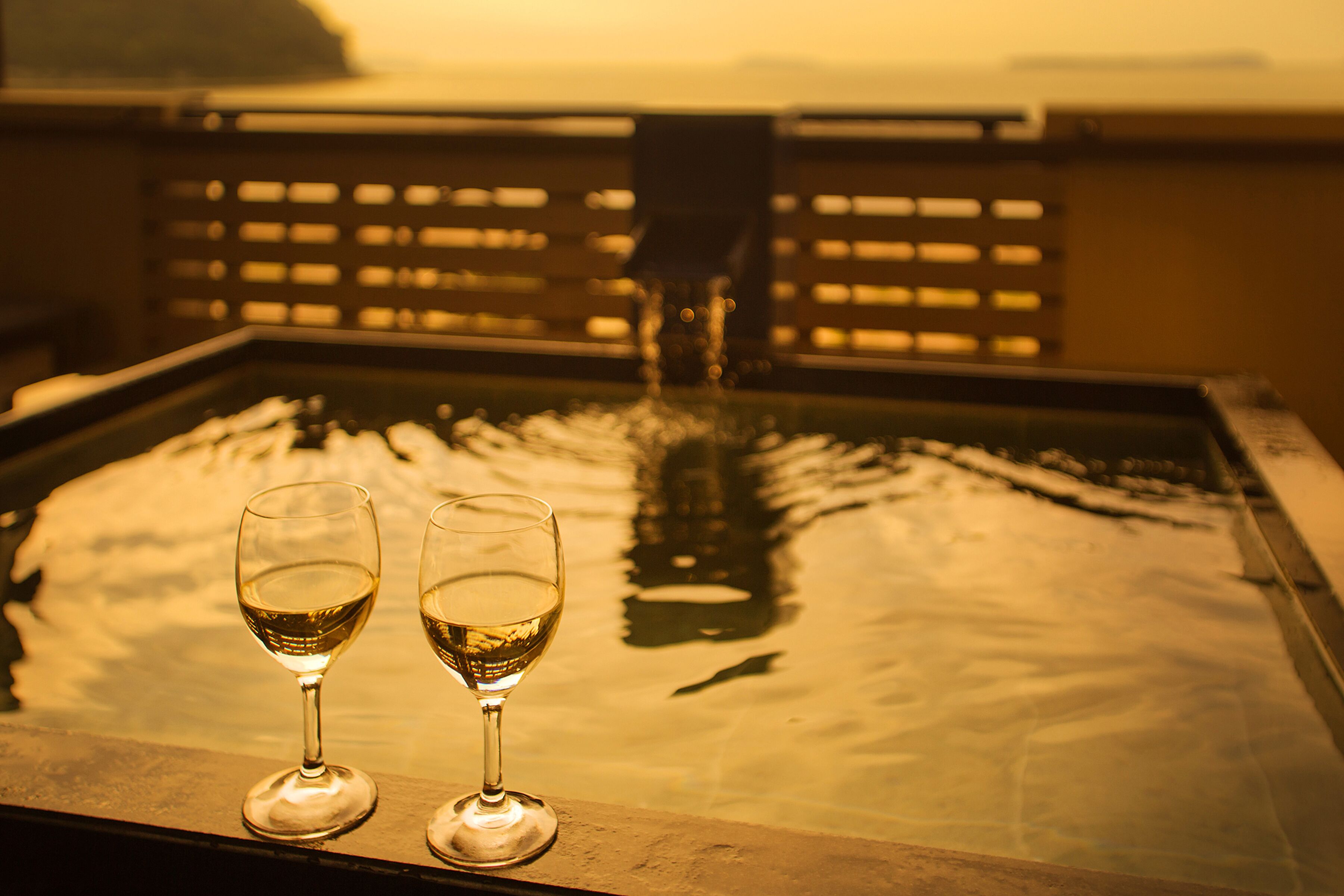 Two glasses of white wine on a reflective surface with a view of a bridge and water in the background.