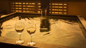 Two glasses of white wine on a reflective surface with a view of a bridge and water in the background.