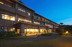 Un hotel de varios pisos con una entrada bien iluminada y un jardín ajardinado.