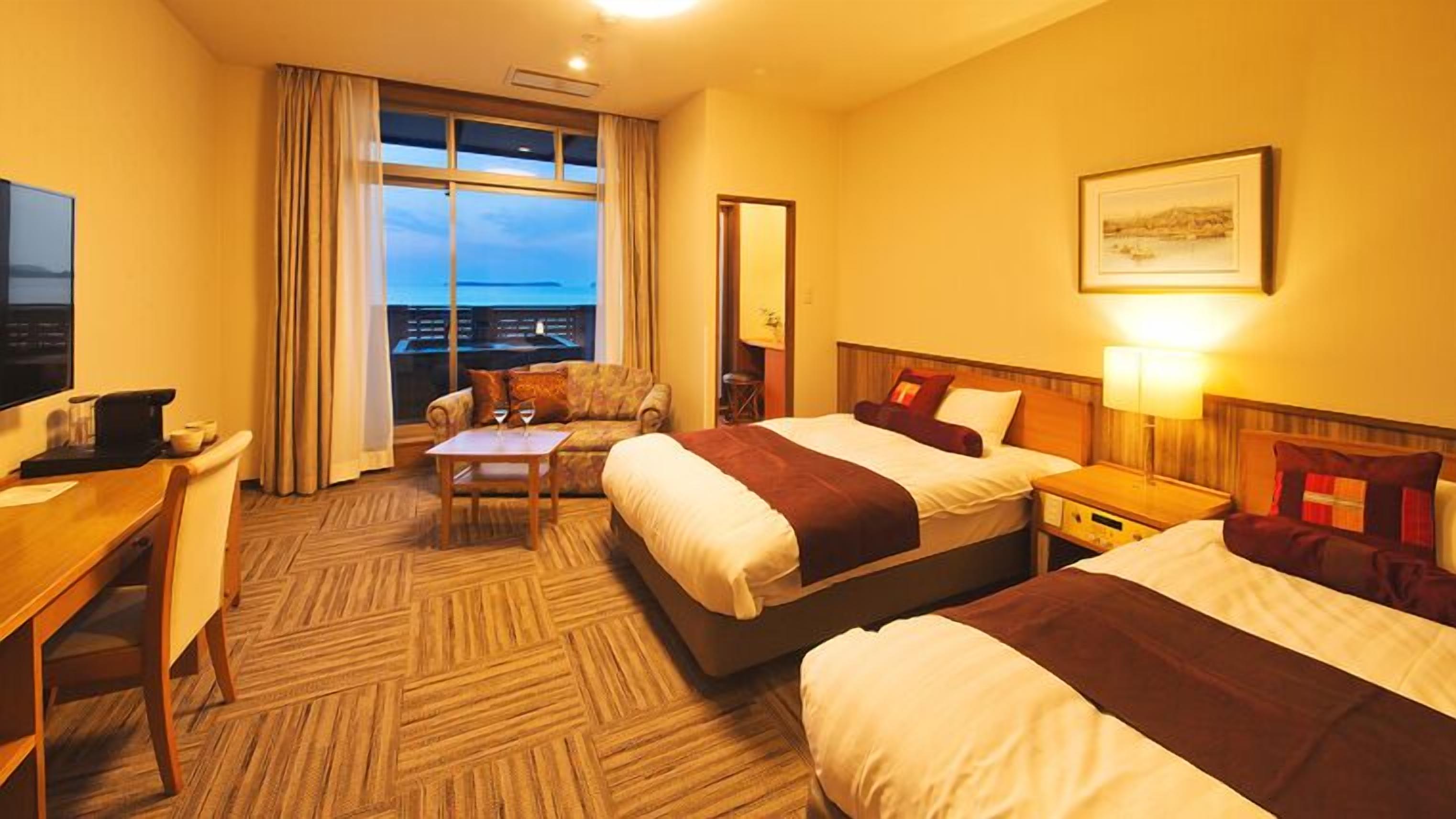 A hotel room with two beds, a desk, a chair, a table, and a large window with a view.