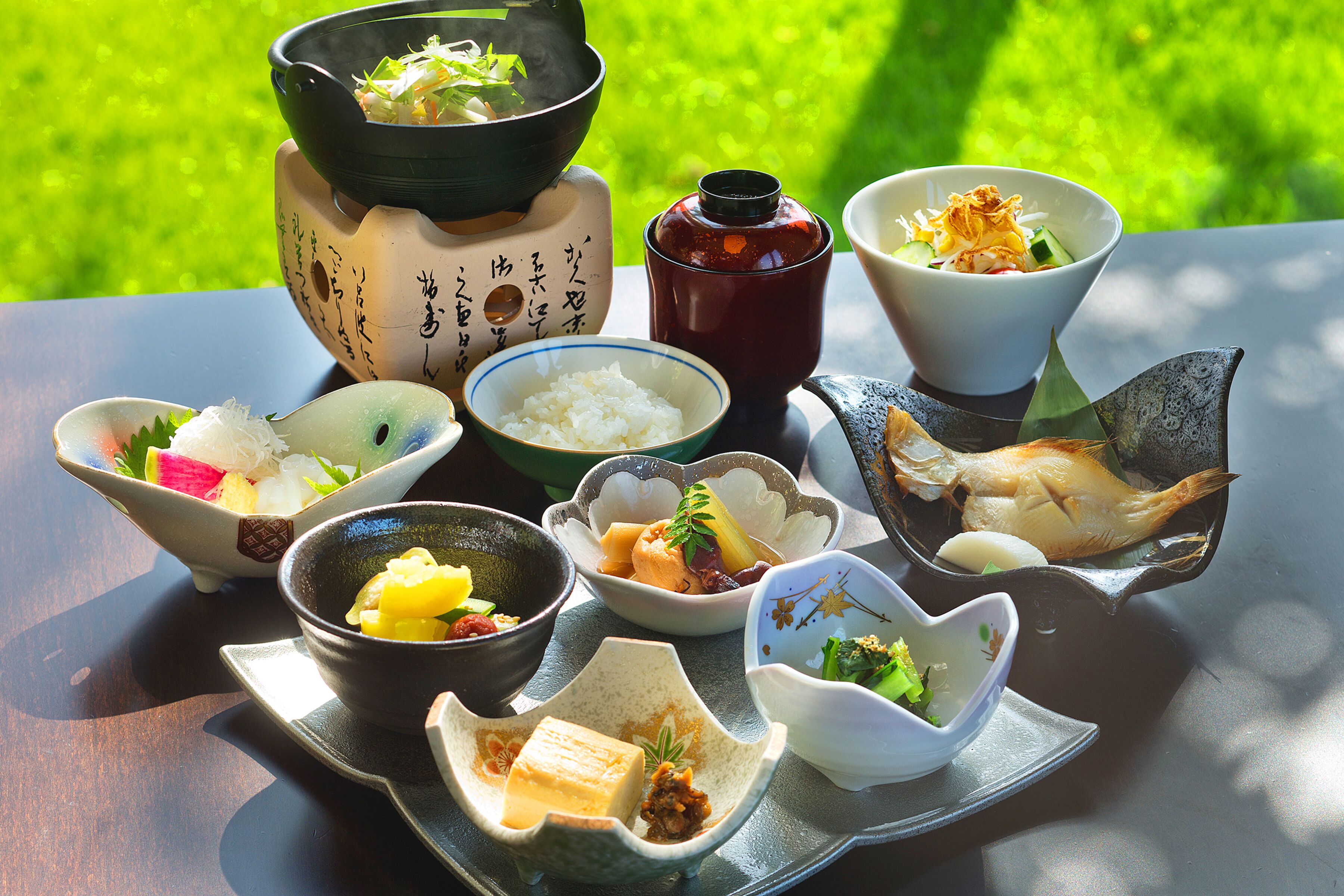 A variety of Japanese dishes arranged on a table outdoors with a green lawn in the background.