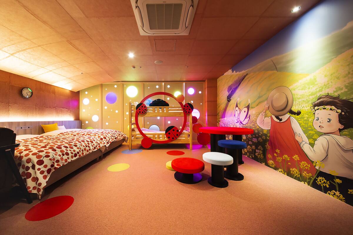 Ein Kinderzimmer mit Etagenbetten, einem Spielbereich mit bunten Hocker und einer Wandmalerei.