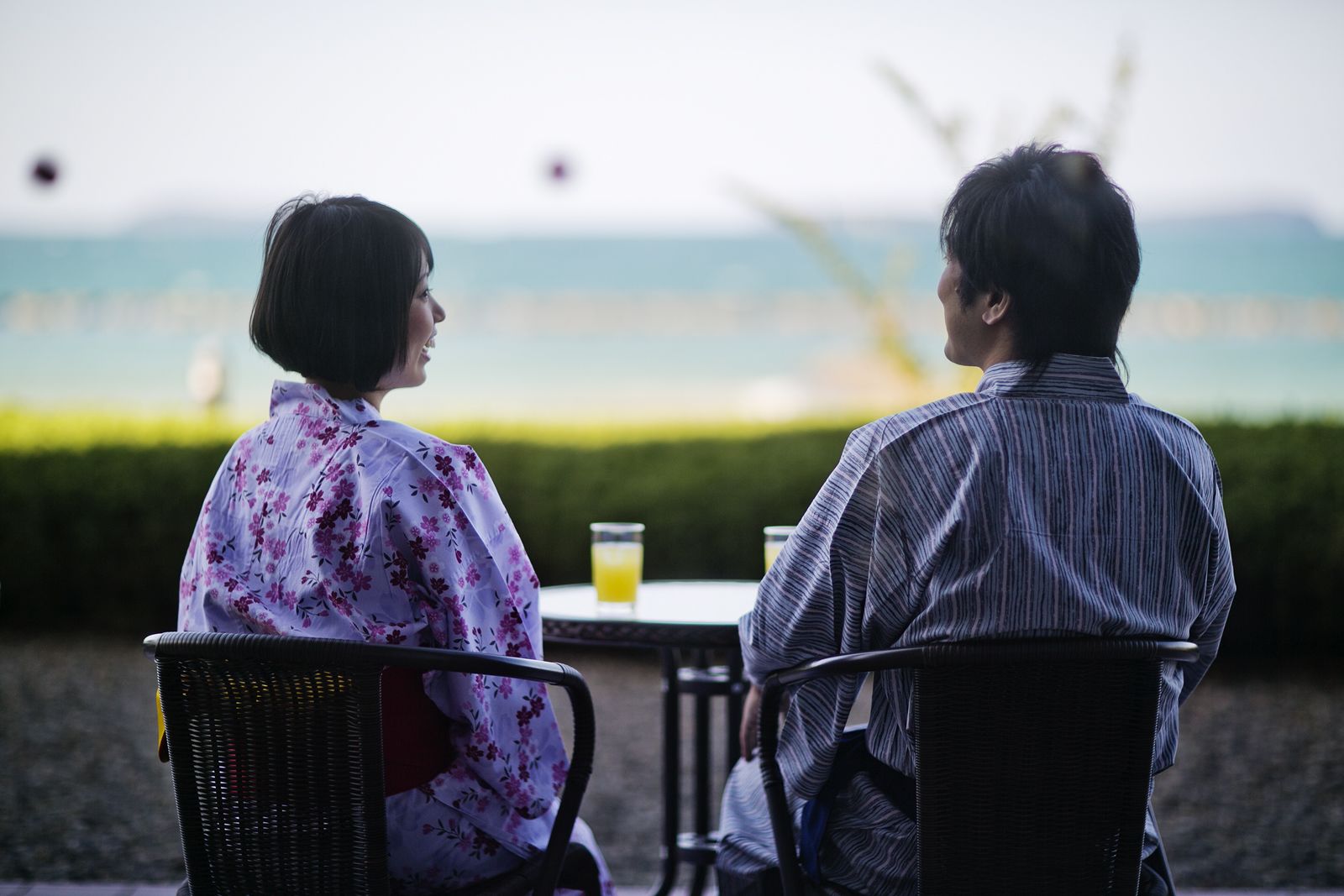 Dos personas sentadas a una mesa con una bebida, con vista a un cuerpo de agua.