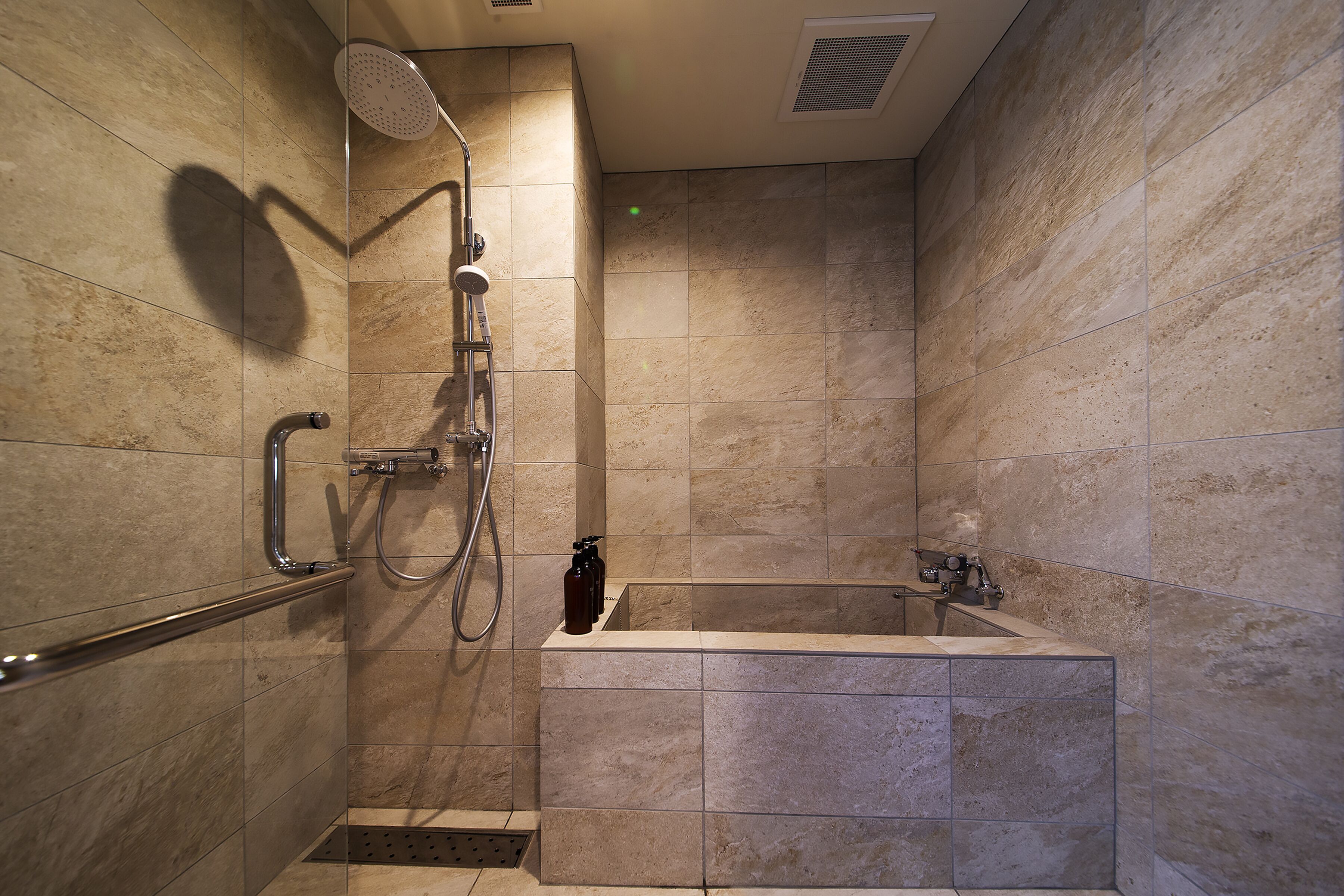A modern bathroom with a shower, a bathtub, and a handrail.