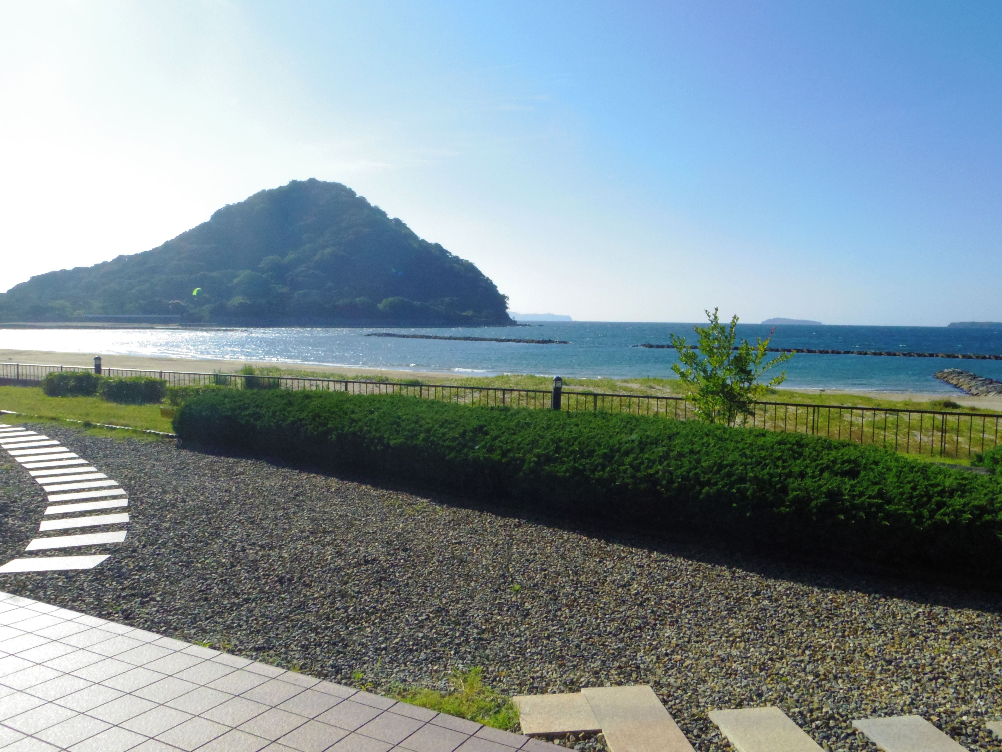 A coastal view with a pebble path, a metal fence, and a distant island.