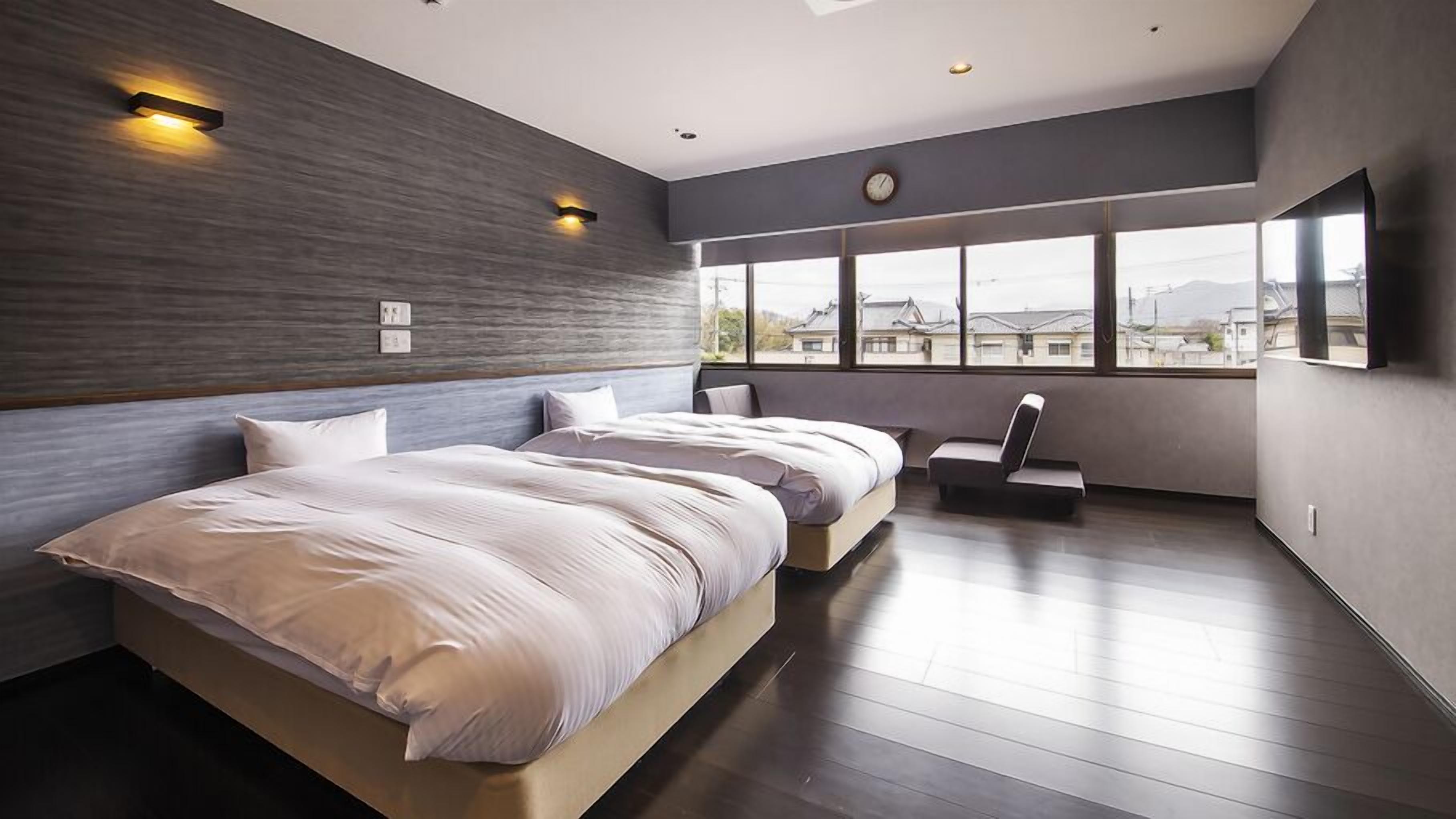A modern bedroom with a large bed, a seating area, and a view of the city through large windows.