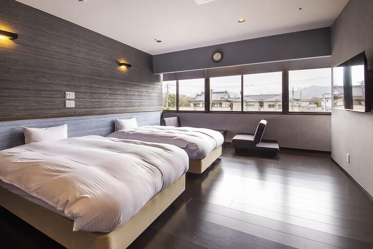 Ein modernes Schlafzimmer mit einem großen Bett, einer Sitzecke und Blick auf die Stadt durch große Fenster.